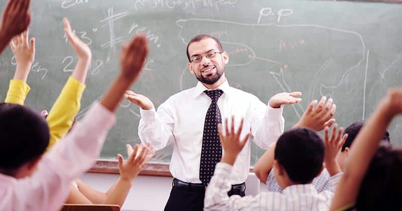 Crowded classroom with many hands up