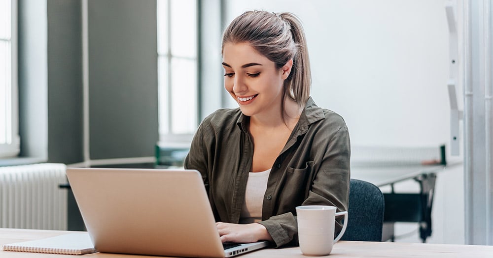 Young woman smiling while typing on a laptop